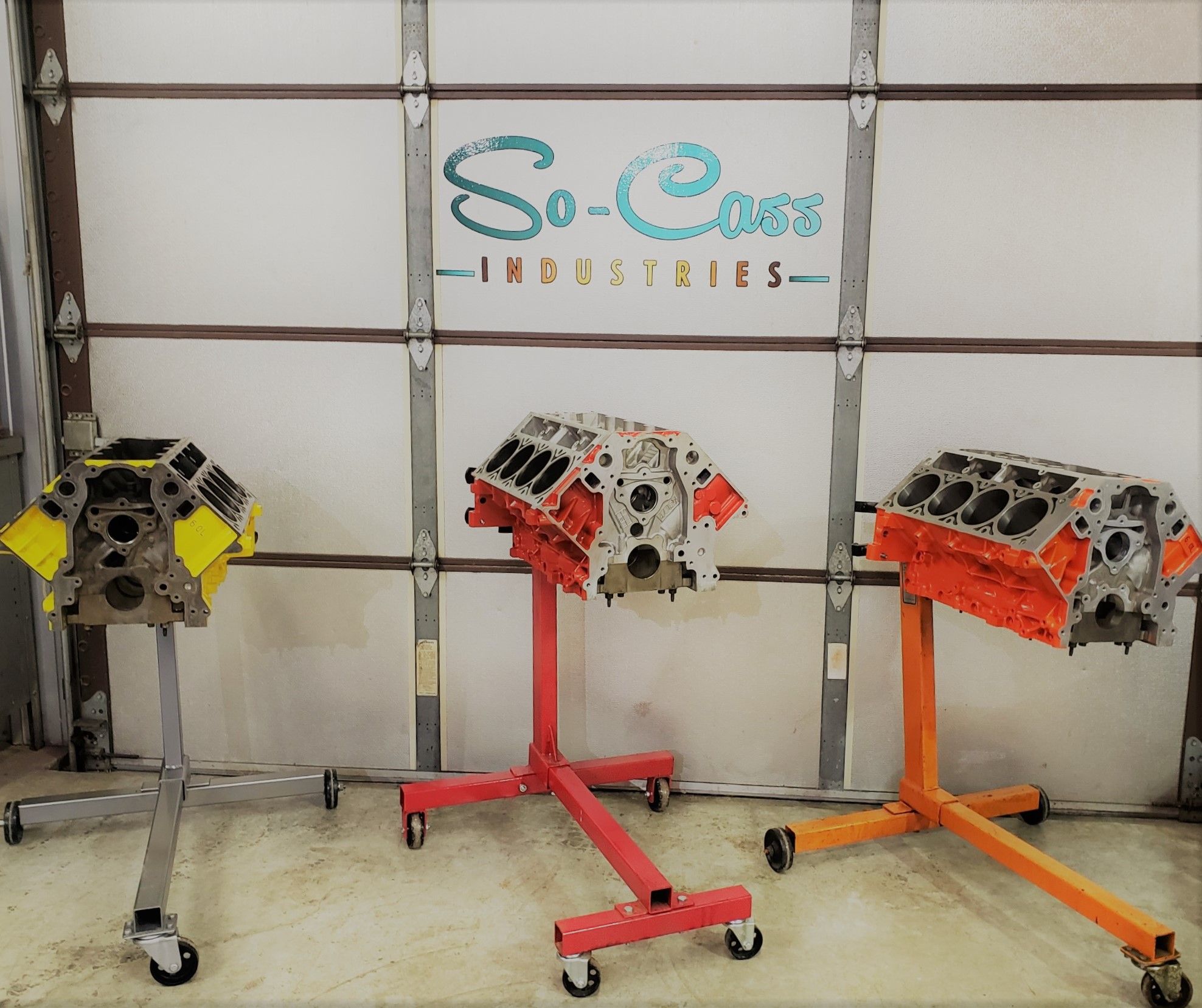 Three engine blocks on rolling stands in front of the garage door painted with the So-Cass Industries wordmark